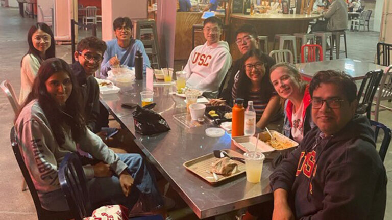 USC Undergraduate Student Consultants (uSCs) and International Teaching Assistants (ITAs) enjoying a meal together at Grand Central Market in Downtown Los Angeles, sitting around a table with food and drinks.